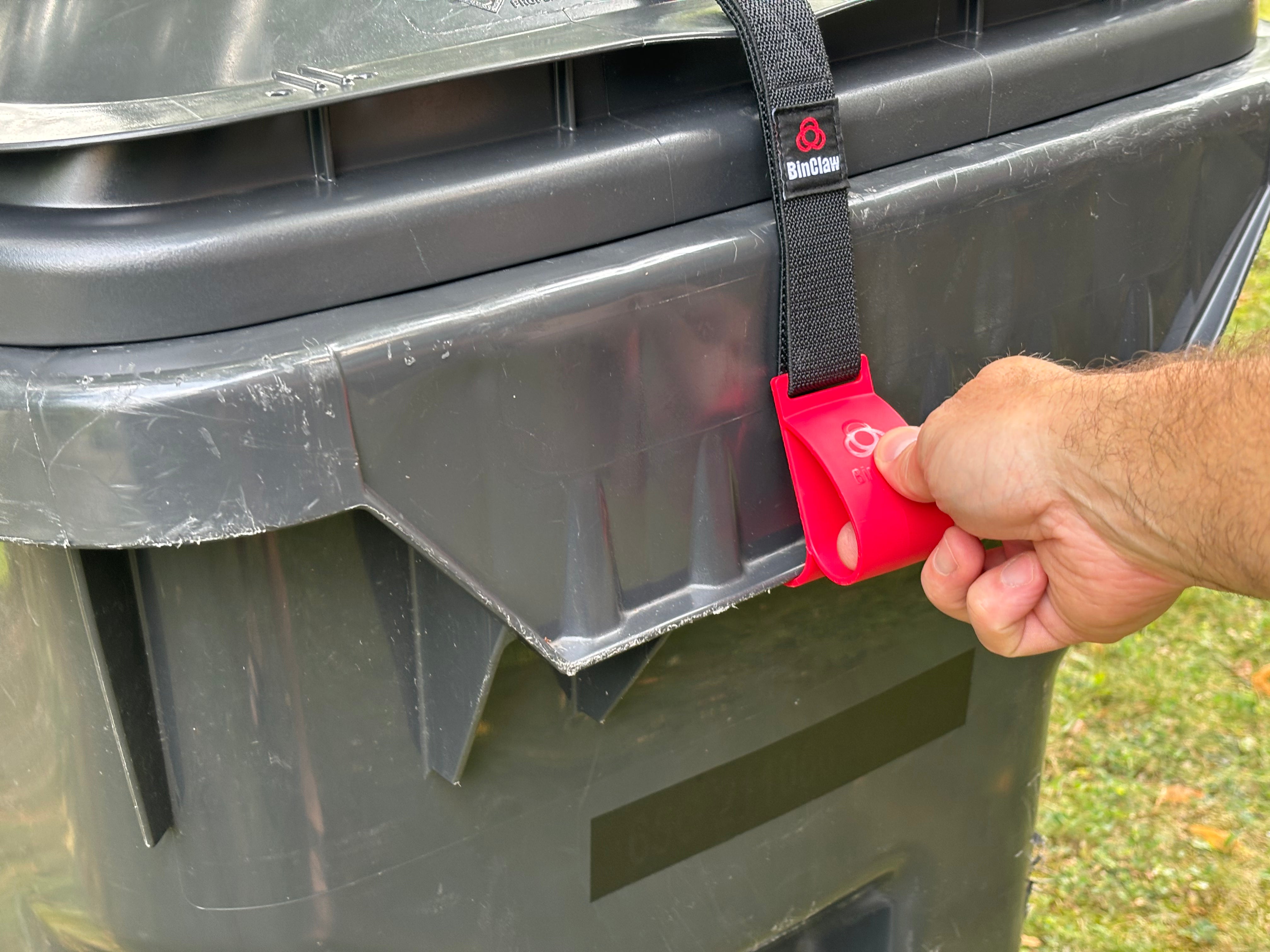 Person using a red BinClaw on a black trash bin
